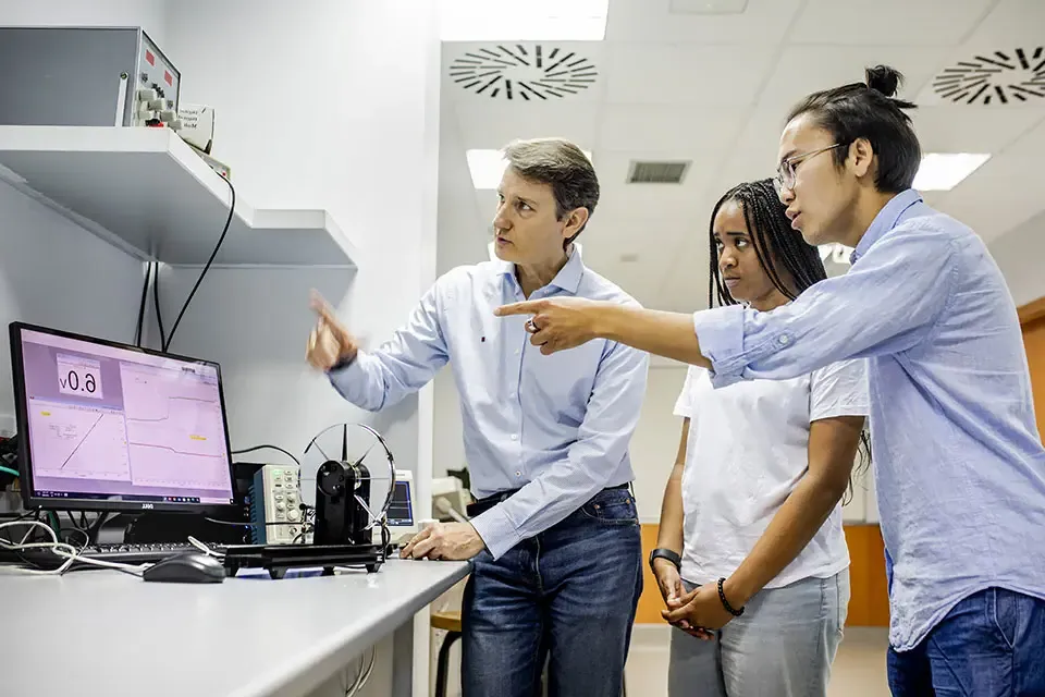 Two students and an instructor examine a computer screen while having a discussion.