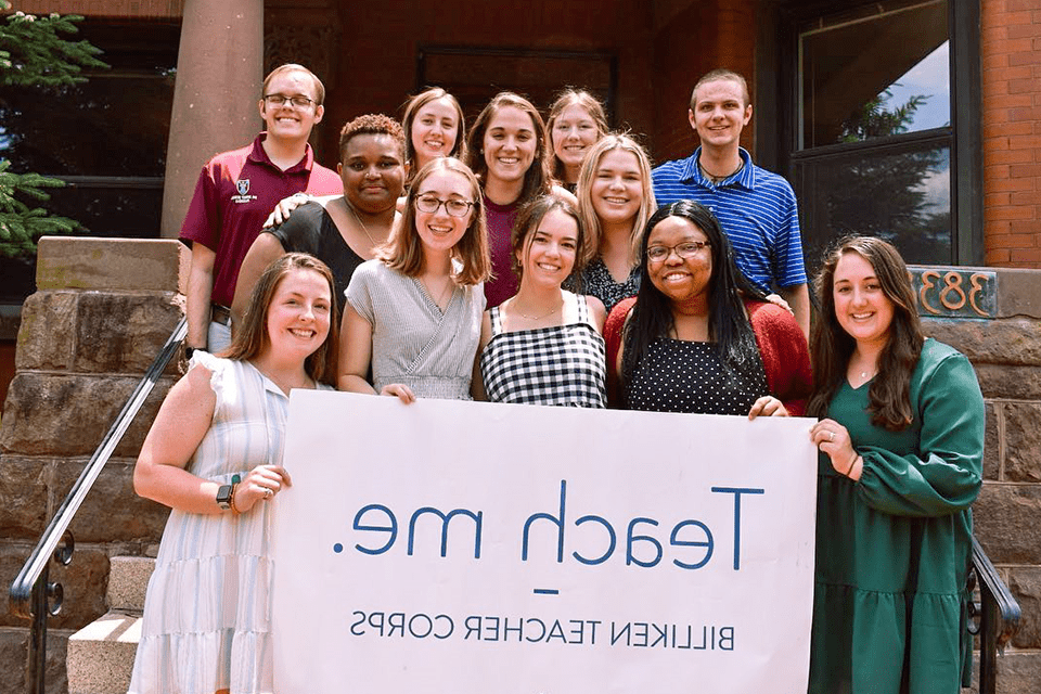 A group photo of students holding a sign that reads "Teach me. Billiken Teacher Corps."