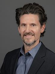 Smiling man in a collared shirt and jacket in front of a blue background